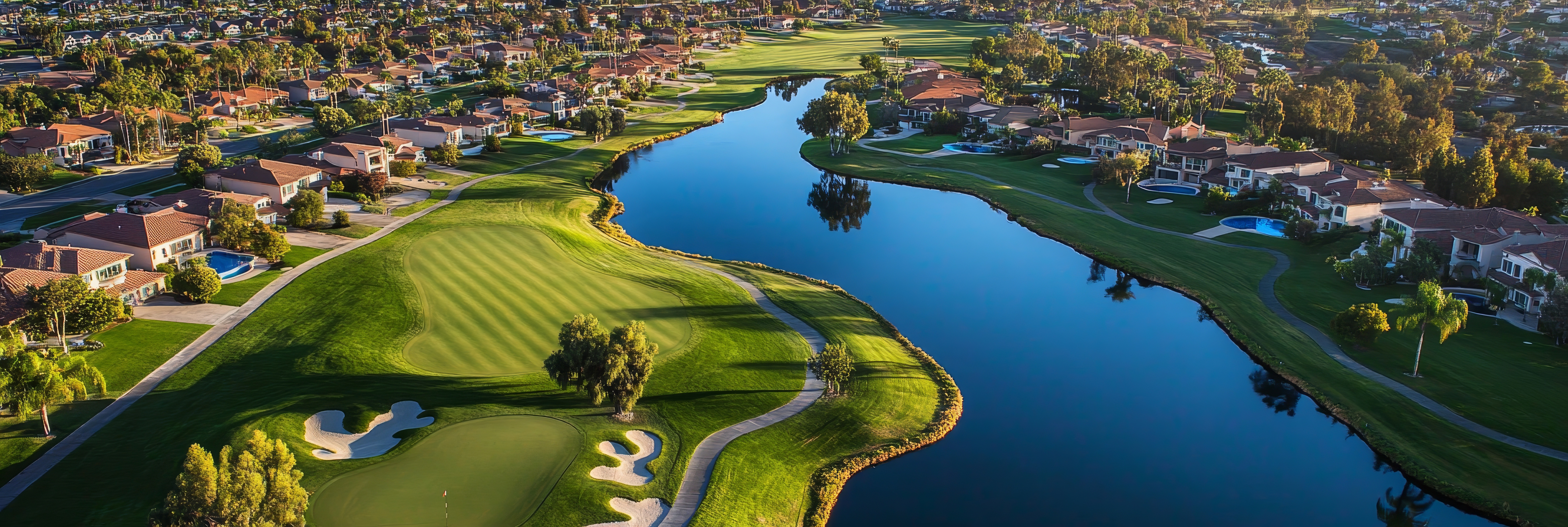An aerial view showcasing a pristine golf course with winding waterways, surrounded by luxurious homes in a tranquil setting. The image embodies luxury, leisure, and natural beauty